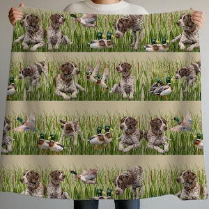 May include: A beige blanket with a repeating pattern of brown and white dogs, ducks, and green reeds. The dogs are in various poses, and the ducks are in the water or flying. The blanket has a soft, inviting appearance.