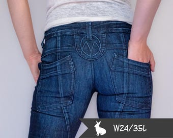 May include: Dark wash denim jeans with a decorative stitched design on the back pockets and a logo on the waistband. The jeans have a W24/35L size label. The person is wearing a white shirt.