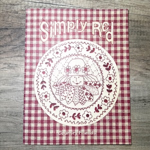 Può includere: Un quaderno con un motivo a quadri rossi e bianchi. La copertina presenta il testo "Simply Red" e un disegno circolare con un'illustrazione di bambola e le parole "Country Friends".