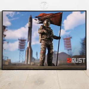 Pode incluir: Pôster emoldurado com um astronauta em um traje espacial desgastado segurando uma bandeira vermelha. Um foguete e um céu azul formam o fundo. A palavra "RUST" é visível no canto inferior direito.