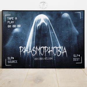May include: A framed poster with a dark blue, grainy background. The word "PHASMOPHOBIA" is in white, dripping font. The image features ghostly figures and timecode details, creating a spooky, cinematic effect.