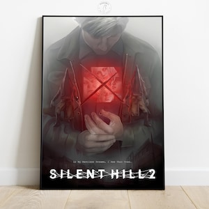 May include: A framed poster featuring artwork from Silent Hill 2. The image shows a person holding a glowing red object with faces inside. The title "SILENT HILL 2" is displayed in white at the bottom, with the quote "In My Restless Dreams, I See That Town..." above it.