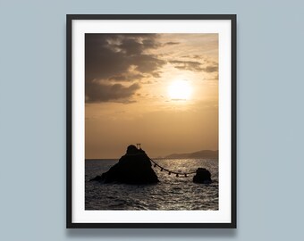 Puede incluir: Fotografía enmarcada de una puesta de sol sobre el océano. El sol es un orbe brillante en el cielo, con nubes oscuras arriba. Rocas silueteadas están en el agua, conectadas por una cuerda con luces. La imagen está enmarcada en un borde negro.