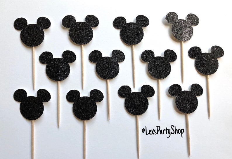 Pode incluir: Doze toppers para cupcake com cabe&ccedil;a de Mickey Mouse em glitter preto em palitos de madeira. Os toppers est&atilde;o dispostos em uma grade sobre um fundo branco.