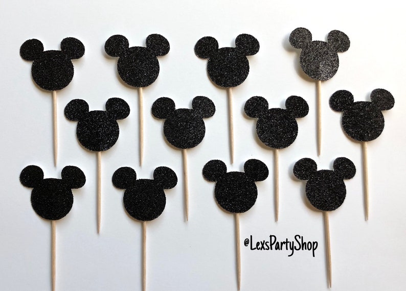 Pode incluir: Doze toppers para cupcakes com a forma de cabe&ccedil;a do Mickey Mouse em glitter preto em palitos de madeira. Os toppers est&atilde;o dispostos em c&iacute;rculo sobre um fundo branco. @LexsPartyShop est&aacute; escrito no canto inferior direito.