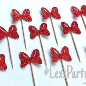 May include: Twelve red glitter bow cupcake toppers on wooden sticks. The bows are all the same size and shape. The background is white. @LexsPartyShop