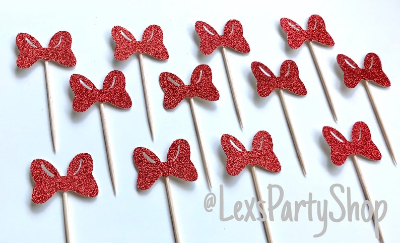 May include: Twelve red glitter bow cupcake toppers on wooden sticks. The bows are all the same size and shape. The background is white. @LexsPartyShop