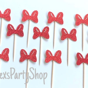 May include: Twelve red glitter bow cupcake toppers on wooden sticks. The bows are all the same size and shape, and they are arranged in a random pattern. The background is white.