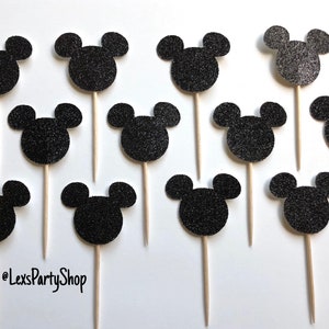 Pode incluir: Doze toppers para cupcakes com a forma de cabe&ccedil;a do Mickey Mouse em glitter preto em palitos de madeira. Os toppers t&ecirc;m um di&acirc;metro de aproximadamente 5 cm.