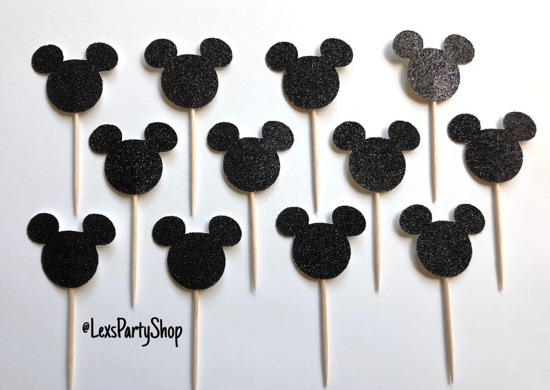 Pode incluir: Doze toppers para cupcakes com a forma de cabe&ccedil;a do Mickey Mouse em glitter preto em palitos de madeira. Os toppers t&ecirc;m um di&acirc;metro de aproximadamente 5 cm.