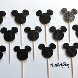 Pode incluir: Doze toppers para cupcakes com a forma de cabe&ccedil;a do Mickey Mouse em glitter preto em palitos de madeira. Os toppers est&atilde;o dispostos em uma grade sobre um fundo branco. @LexsPartyShop