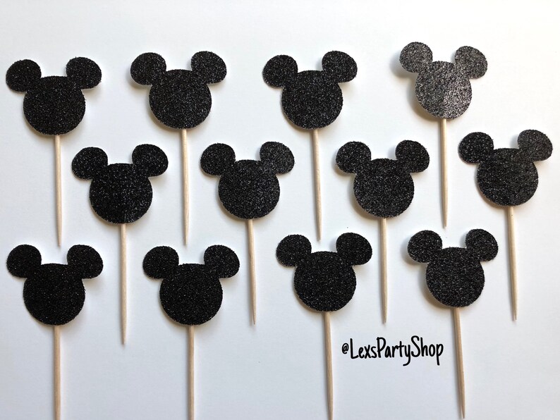 Pode incluir: Doze toppers para cupcakes com a forma de cabe&ccedil;a do Mickey Mouse em glitter preto em palitos de madeira. Os toppers est&atilde;o dispostos em uma grade sobre um fundo branco. @LexsPartyShop