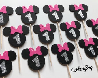 May include: Twelve black and pink Minnie Mouse themed cupcake toppers with a silver glitter number one on each. The toppers are on wooden skewers.