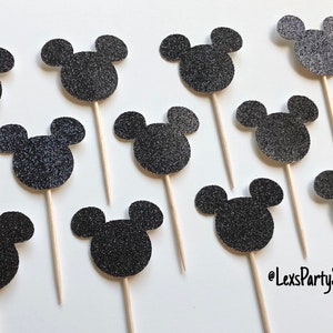 Pode incluir: Doze toppers para cupcakes com a forma da cabe&ccedil;a do Mickey Mouse em glitter preto em palitos de madeira. Os toppers t&ecirc;m um di&acirc;metro de aproximadamente 5 cm.