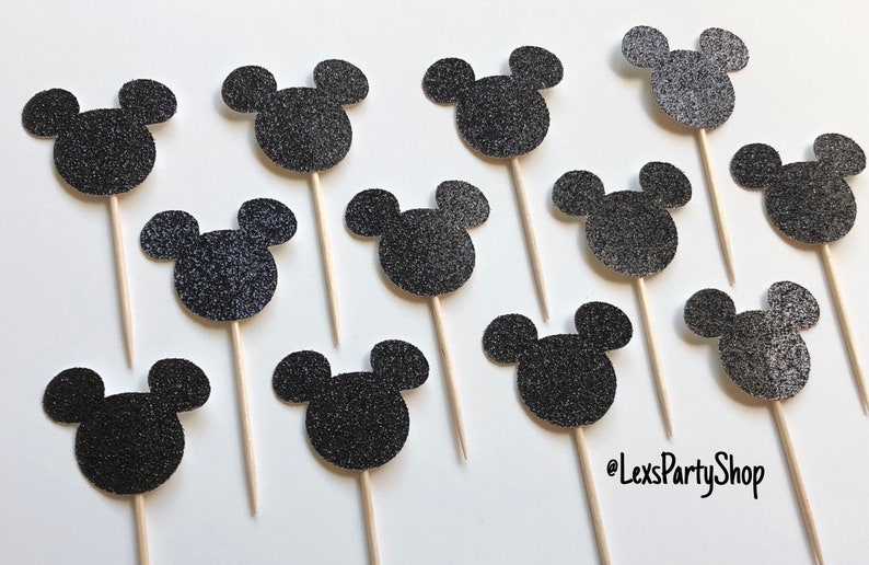 Pode incluir: Doze toppers para cupcakes com a forma da cabe&ccedil;a do Mickey Mouse em glitter preto em palitos de madeira. Os toppers t&ecirc;m um di&acirc;metro de aproximadamente 5 cm.