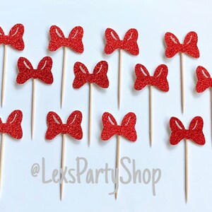 May include: Twelve red glitter bow cupcake toppers on wooden sticks. The bows are all the same size and shape, and they are arranged in a random pattern. The text "@LexsPartyShop" is visible in the bottom center of the image.