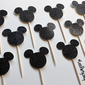 Pode incluir: Toppers para cupcake com cabe&ccedil;a de Mickey Mouse de glitter preto. Existem 12 toppers na imagem. Os toppers est&atilde;o em palitos de madeira.