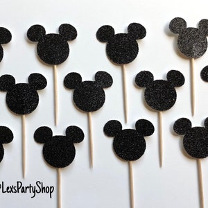 Pode incluir: Doze toppers para cupcakes com a forma da cabe&ccedil;a do Mickey Mouse em glitter preto em palitos de madeira. Os toppers est&atilde;o dispostos em forma de grade sobre um fundo branco. O texto "@LexsPartyShop" est&aacute; no canto inferior esquerdo da imagem.