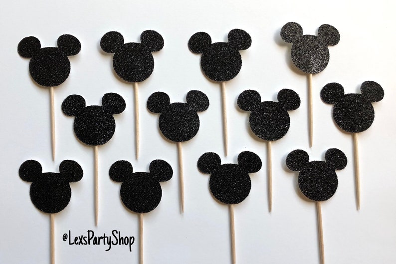 Pode incluir: Doze toppers para cupcakes com a forma da cabe&ccedil;a do Mickey Mouse em glitter preto em palitos de madeira. Os toppers est&atilde;o dispostos em forma de grade sobre um fundo branco. O texto "@LexsPartyShop" est&aacute; no canto inferior esquerdo da imagem.