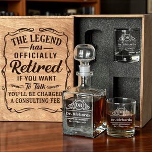 Può includere: Un set regalo in legno con una caraffa, due bicchieri e una scatola di legno. La caraffa e i bicchieri sono incisi con "Dr. Richards" e "Happy Retirement!". La scatola recita "The Legend has Officially Retired".