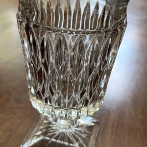 May include: Clear glass goblet with a square base and a textured, diamond-patterned body. The rim is slightly flared, and the glass has a vintage aesthetic. The goblet is likely used for serving beverages.