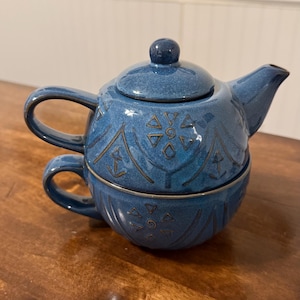 Könnte beinhalten: Ein blaues Keramik-Teeservice mit einer Teekanne und einer Tasse. Die Teekanne hat einen Deckel und einen Ausguss, und die Tasse passt darunter. Das Set ist mit einem nautischen Muster in dunklerem Blau verziert.