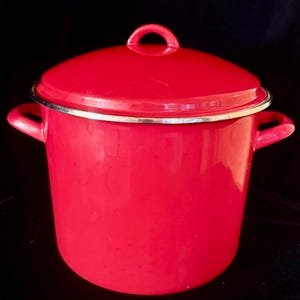 Pode incluir: Uma panela de esmalte vermelho brilhante com tampa a condizer e duas pegas laterais. A panela apresenta um acabamento liso e brilhante e um rebordo de metal prateado na parte superior onde a tampa assenta. A tampa tem uma pequena pega arqueada.