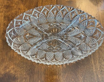 May include: Clear, oval-shaped glass serving dish with a divided design. The dish features intricate star and geometric patterns throughout, with a scalloped edge. Ideal for serving snacks or appetizers.
