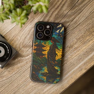 May include: A black smartphone case featuring a stained-glass style illustration of a woman in a traditional Japanese outfit, standing near a pagoda and water. The case has a black border and a multi-lens camera cutout.