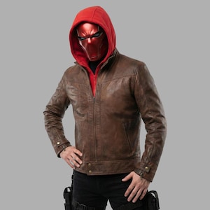 May include: A brown leather jacket with a textured pattern, worn over a red hooded sweatshirt. The jacket has a zipper closure and two front pockets. The person is wearing a red helmet with a visor.