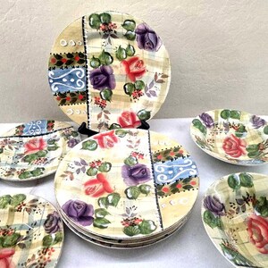 May include: A set of round ceramic plates and bowls featuring a cream-colored background with a plaid pattern, decorated with painted red and purple roses, green leaves, and a vertical blue and red decorative border with white circular accents.
