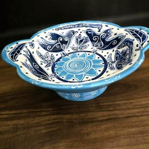 May include: A ceramic bowl with a blue and white floral and bird design. The bowl has a scalloped edge and a pedestal base. The words "everyday is special" and "life is" are written on the rim of the bowl.