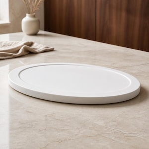 May include: A smooth, matte white oval tray with a raised outer rim. The tray features a clean, solid surface and a simple, uniform design. It is a flat, elliptical object with a consistent white finish, presenting a neutral and functional appearance.