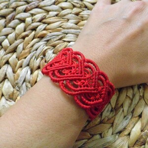 Puede incluir: Un brazalete de macram&eacute; rojo con un dise&ntilde;o de coraz&oacute;n.