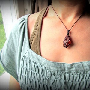 May include: A close-up of a woman wearing a light blue, ruffled top and a necklace with a brown cord and a large, orange, faceted gemstone pendant.