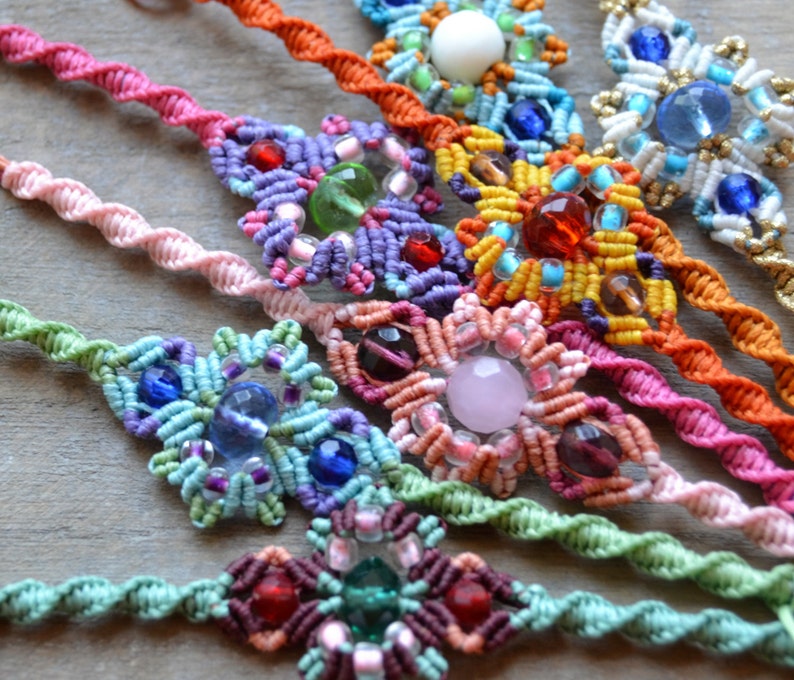 Puede incluir: Una colecci&oacute;n de pulseras de amistad coloridas con intrincados nudos y diversas cuentas, incluyendo cuentas rosas, moradas, verdes, azules, naranjas y blancas.