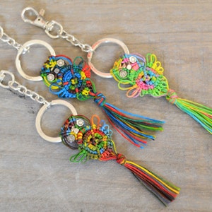 Pode incluir: Tr&ecirc;s chaveiros coloridos com argolas de prata. Cada chaveiro apresenta um design de n&oacute; em forma de borla com uma variedade de cores, incluindo verde, azul, vermelho, amarelo e preto. Os chaveiros s&atilde;o feitos com uma t&eacute;cnica de macram&eacute;.