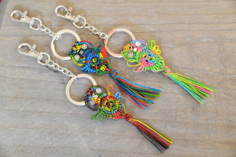 Pode incluir: Tr&ecirc;s chaveiros coloridos com argolas de prata. Cada chaveiro apresenta um design de n&oacute; em forma de borla com uma variedade de cores, incluindo verde, azul, vermelho, amarelo e preto. Os chaveiros s&atilde;o feitos com uma t&eacute;cnica de macram&eacute;.