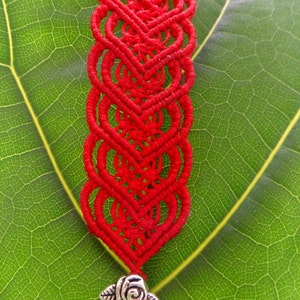 Puede incluir: Pulsera de macram&eacute; roja con un cierre plateado con dise&ntilde;o de rosa.