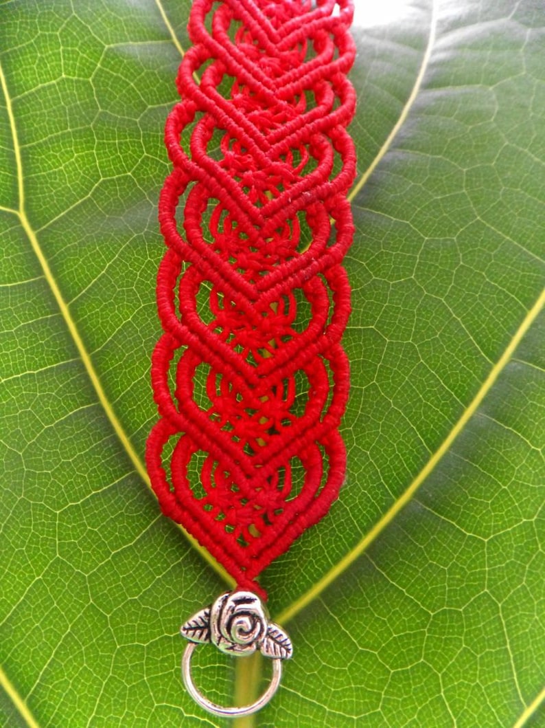 Puede incluir: Pulsera de macram&eacute; roja con un cierre plateado con dise&ntilde;o de rosa.