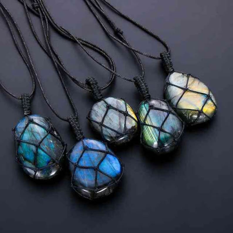 May include: Five necklaces with black cords and iridescent gemstone pendants wrapped in macrame. The gemstones are various shades of blue, green, and gold.