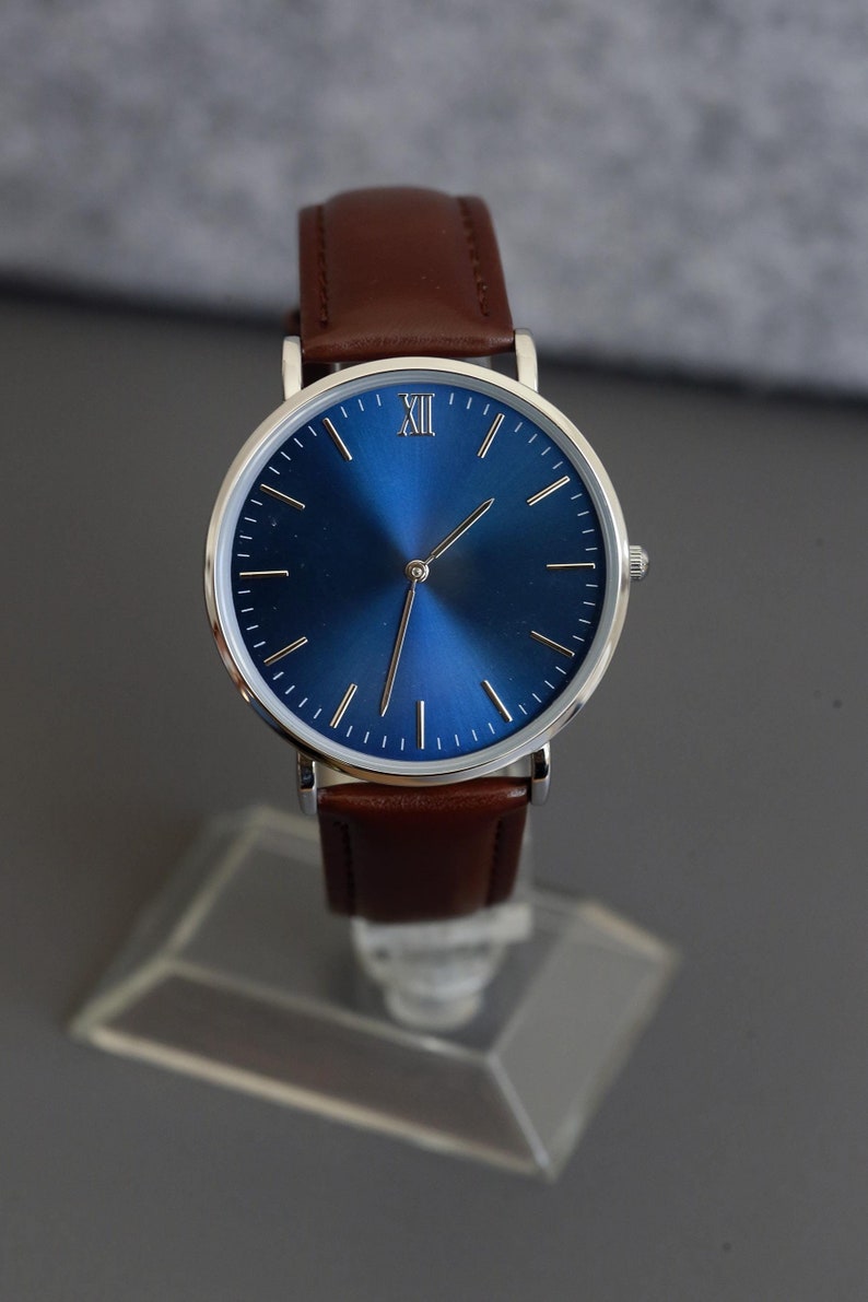 May include: A silver watch with a blue face and Roman numeral hour markers. The watch has a brown leather band.