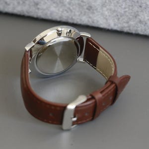 May include: A silver watch with a brown leather band. The watch face is not visible in the image.