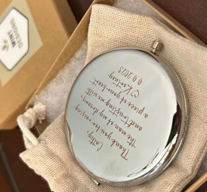 Op de afbeelding: Een zilveren compact spiegel met een handgeschreven bericht dat luidt: "Cattry, Dank je voor het opvoeden van de man van mijn dromen, en voor het vertrouwen dat je me geeft met een deel van je hart. Kartney 9.9.2023"