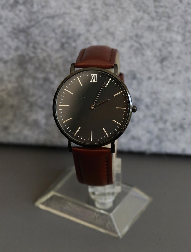 May include: A black analog wristwatch with a brown leather band. The watch face has Roman numeral hour markers and a black background.
