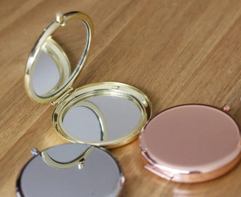 Op de afbeelding: Drie compacte spiegels, &eacute;&eacute;n goudkleurig met een scharnierend deksel, &eacute;&eacute;n goudkleurig en &eacute;&eacute;n ros&eacute; goudkleurig. De spiegels zijn rond en hebben een reflecterend oppervlak.
