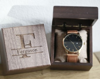 May include: A wooden box with a personalized engraved initial "E" and the name "Ferguson" on the lid. The box contains a gold-tone wristwatch with a black face and a brown leather band.