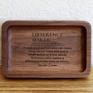 May include: A wooden tray with a quote about a difference maker engraved on it. The quote reads: "A dedicated person who can make a big impact even with just a small action or a few words. Someone who makes a difference in the lives of others. See also: Emma"