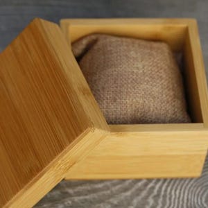 May include: A light brown wooden box with a lid. The box is open and has a brown fabric cushion inside.