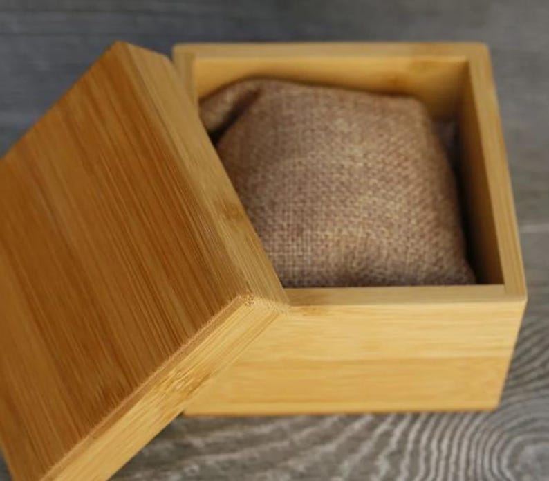 May include: A light brown wooden box with a lid. The box is open and has a brown fabric cushion inside.